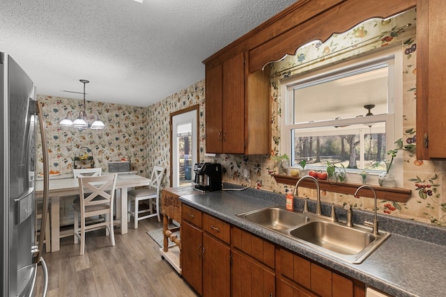 kitchen with a textured ceiling, a sink, stainless steel fridge with ice dispenser, dark countertops, and wallpapered walls