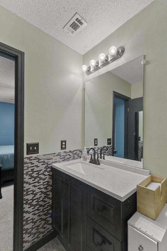 bathroom with a textured ceiling, vanity, visible vents, tile walls, and wainscoting