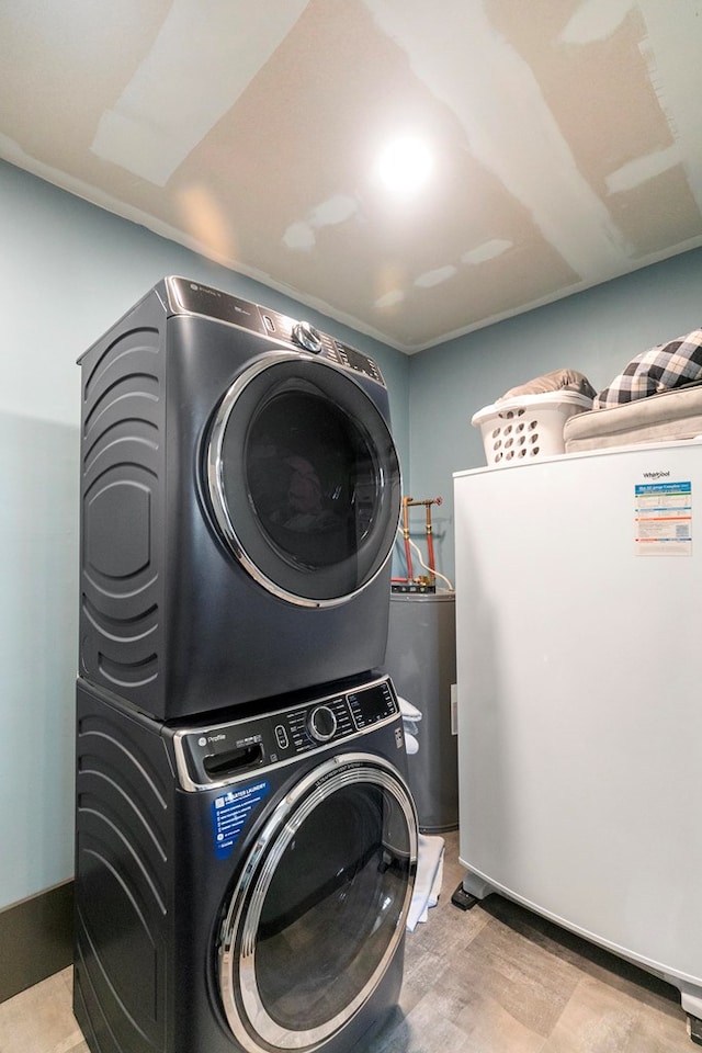 laundry room featuring water heater, laundry area, light wood finished floors, and stacked washer / dryer