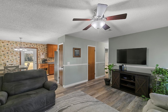 living area featuring visible vents, a textured ceiling, light wood-type flooring, baseboards, and ceiling fan with notable chandelier