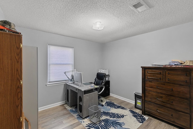 office space with a textured ceiling, light wood-type flooring, visible vents, and baseboards