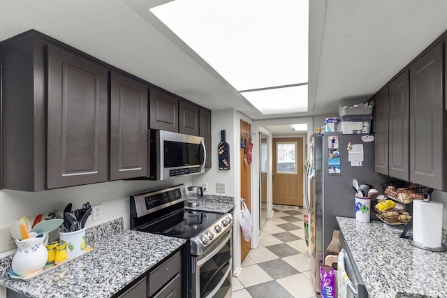 kitchen featuring light floors, appliances with stainless steel finishes, dark brown cabinetry, and light stone countertops