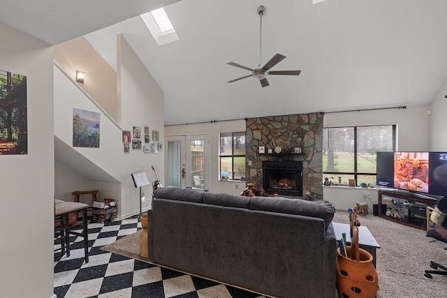 living area with high vaulted ceiling, a stone fireplace, a skylight, a ceiling fan, and light floors