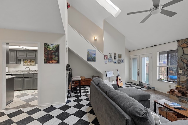 living room with vaulted ceiling with skylight, a ceiling fan, baseboards, french doors, and light floors