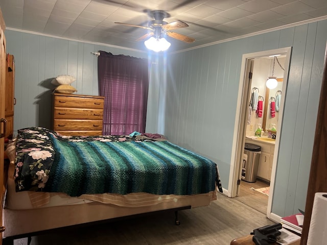 bedroom featuring connected bathroom, ceiling fan, light hardwood / wood-style floors, wooden walls, and ornamental molding