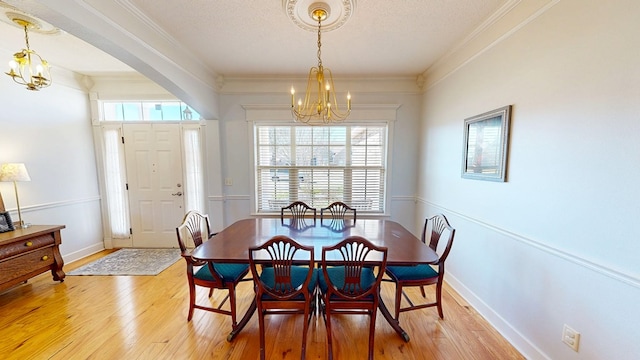 dining room with ornamental molding, light wood-style flooring, baseboards, and an inviting chandelier