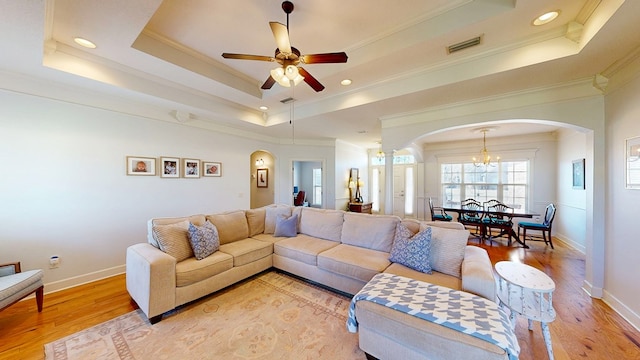 living area with light wood-style flooring, a tray ceiling, visible vents, and arched walkways