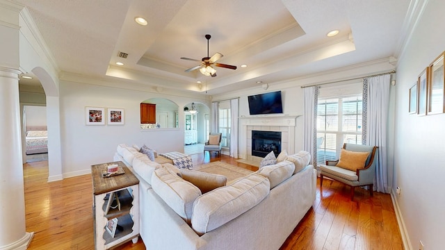 living room with light wood-style floors, arched walkways, a raised ceiling, and visible vents