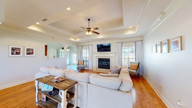 living area with light wood-style flooring, a raised ceiling, and crown molding