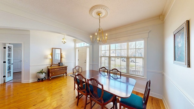 dining area featuring arched walkways, a textured ceiling, light wood-style flooring, an inviting chandelier, and crown molding