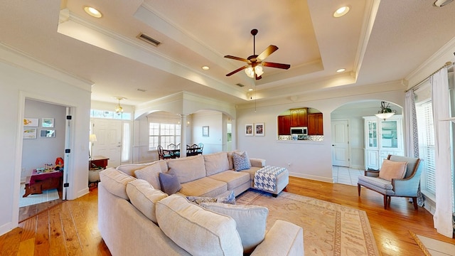 living area with light wood-type flooring, visible vents, arched walkways, and a raised ceiling