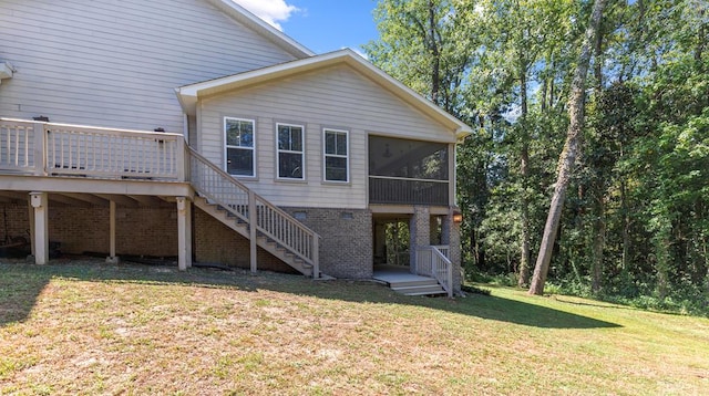 back of property featuring a lawn, a sunroom, stairway, a deck, and brick siding