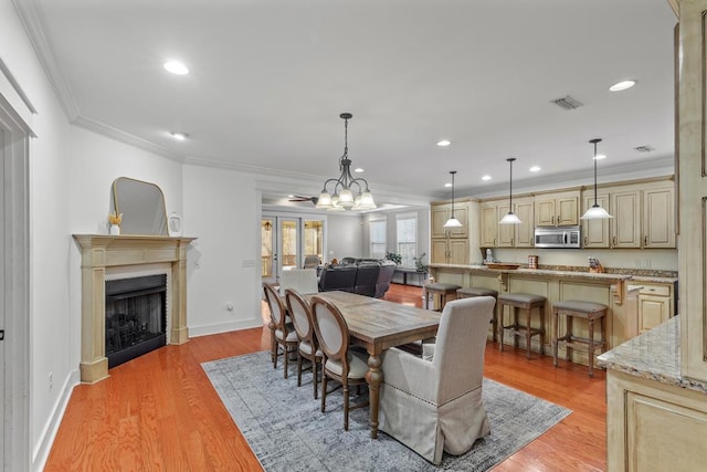 dining room featuring visible vents, crown molding, light wood-style flooring, and a fireplace