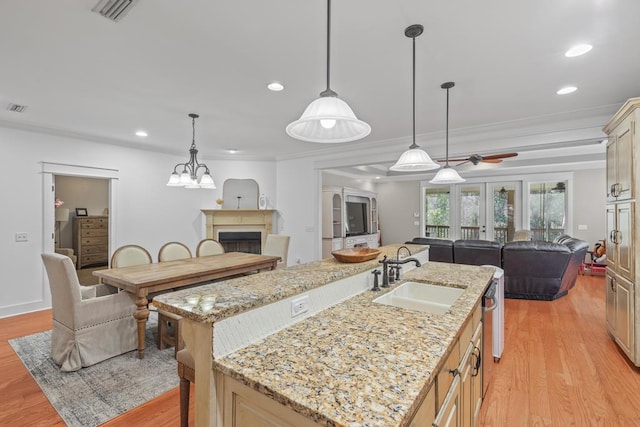 kitchen with a fireplace, a center island with sink, light wood-style flooring, open floor plan, and a sink