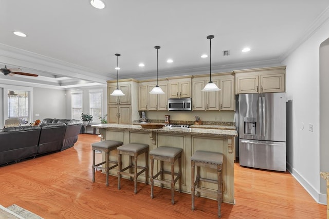 kitchen featuring cream cabinets, appliances with stainless steel finishes, a breakfast bar area, and ornamental molding