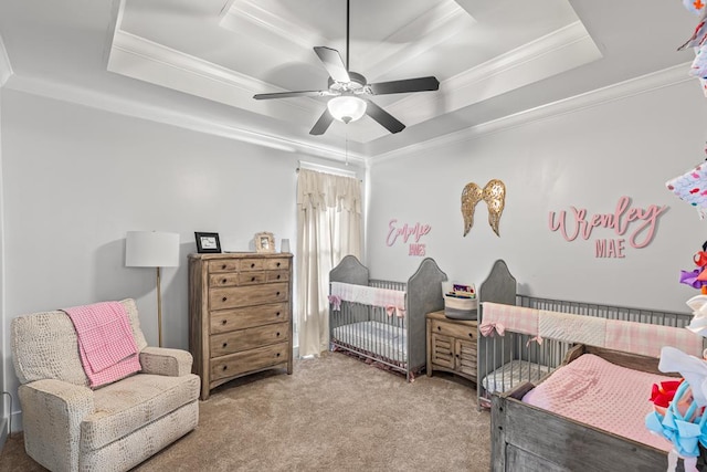 carpeted bedroom featuring ornamental molding, a tray ceiling, a crib, and a ceiling fan