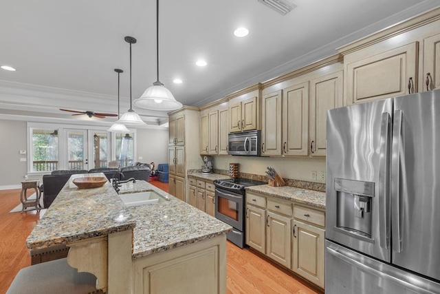 kitchen featuring stainless steel appliances, light wood-style flooring, cream cabinets, open floor plan, and a kitchen breakfast bar