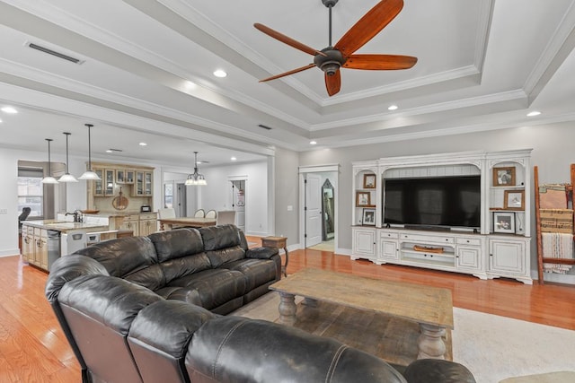 living room with light wood-style flooring, visible vents, a raised ceiling, and ornamental molding