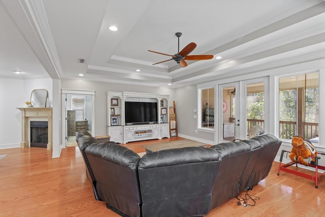 living area with crown molding, a fireplace, a raised ceiling, and light wood-style floors