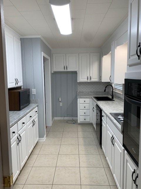 kitchen featuring black appliances, sink, light tile patterned floors, white cabinets, and decorative backsplash