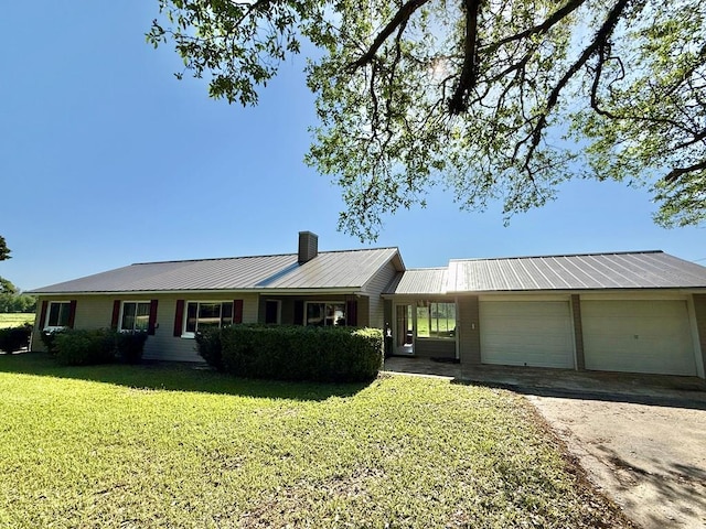 ranch-style house featuring a chimney, driveway, a front lawn, a garage, and metal roof