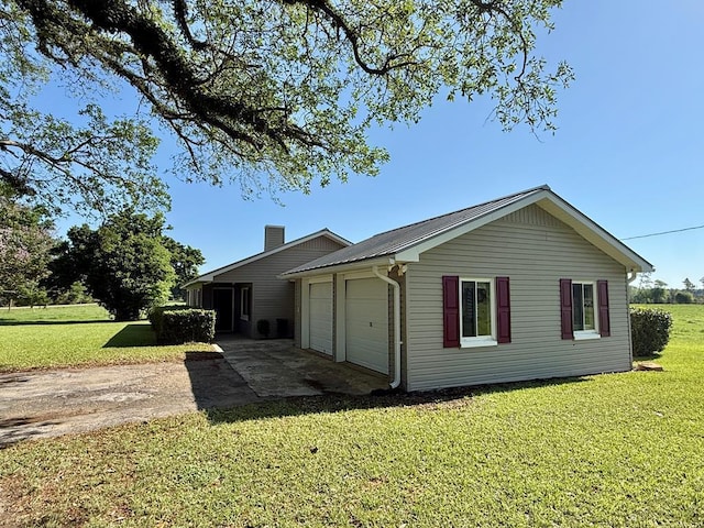 view of side of home with metal roof, a garage, a lawn, and a chimney