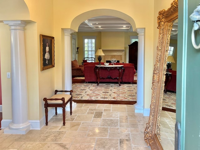 hallway featuring arched walkways, coffered ceiling, decorative columns, and stone tile floors