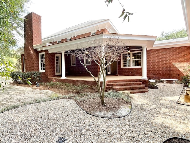 back of house with covered porch, brick siding, and a chimney