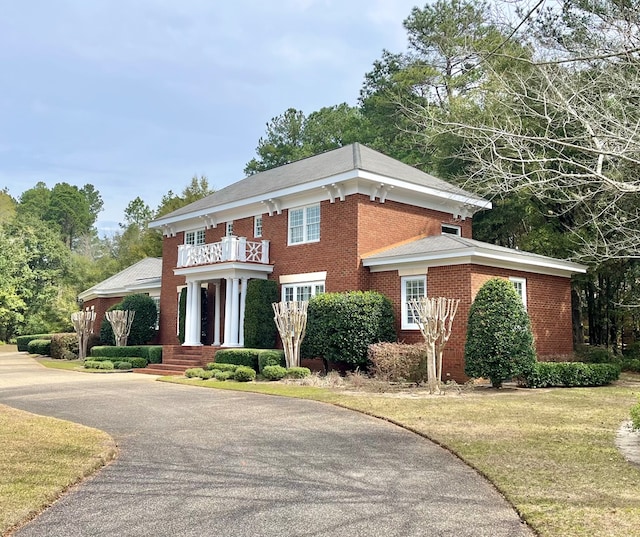 view of front of house with brick siding, a front lawn, and a balcony