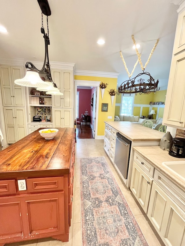 kitchen with light tile patterned floors, butcher block countertops, hanging light fixtures, crown molding, and stainless steel dishwasher