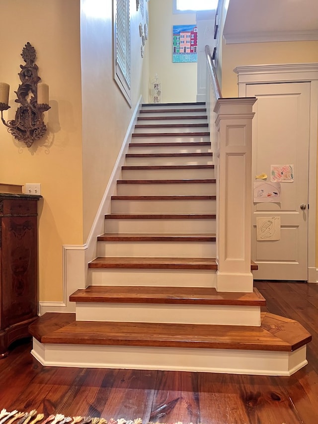 staircase with ornamental molding, wood finished floors, and baseboards