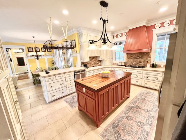 kitchen featuring butcher block countertops, stainless steel dishwasher, premium range hood, gas cooktop, and a notable chandelier