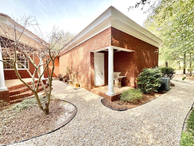 view of property exterior featuring central AC unit, brick siding, and a patio area