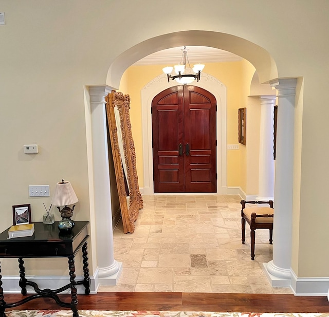 corridor featuring baseboards, arched walkways, decorative columns, and stone tile floors