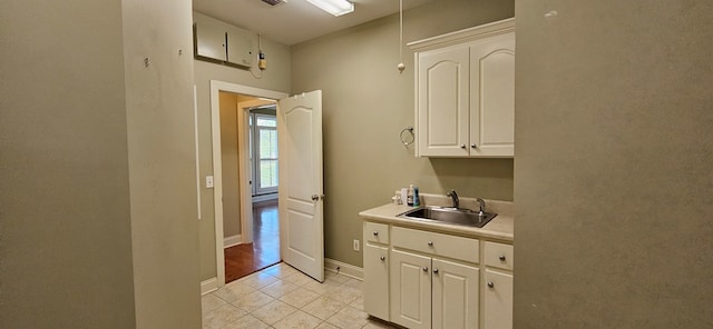 kitchen with a sink, white cabinetry, light countertops, light tile patterned floors, and baseboards