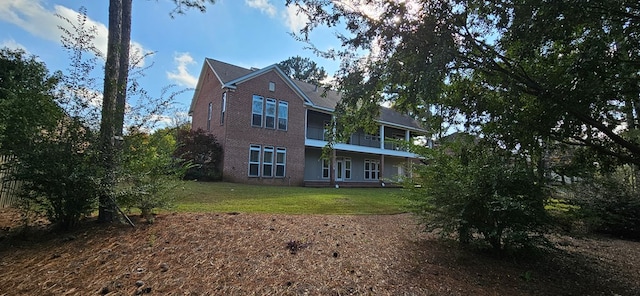 back of property with a balcony, a yard, and brick siding