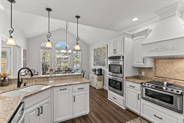 kitchen with custom exhaust hood, hanging light fixtures, appliances with stainless steel finishes, white cabinets, and a sink