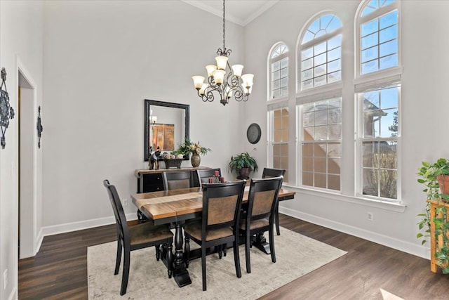 dining room featuring dark wood-style flooring, a notable chandelier, a towering ceiling, ornamental molding, and baseboards