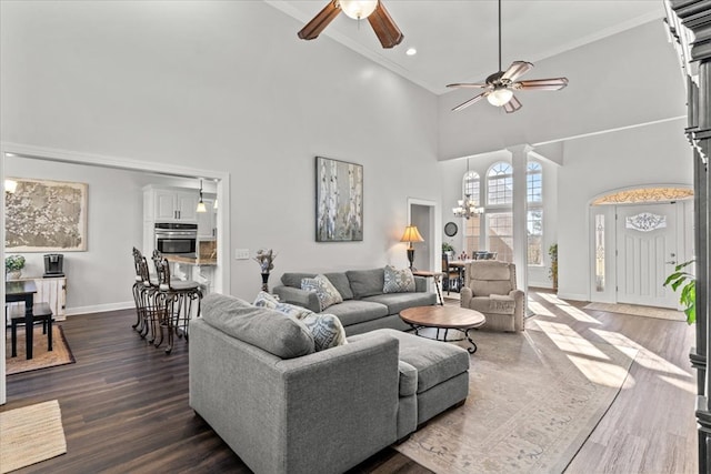 living room with ceiling fan with notable chandelier, baseboards, ornamental molding, dark wood-style floors, and decorative columns