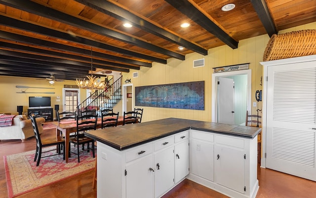 kitchen with kitchen peninsula, ceiling fan with notable chandelier, beam ceiling, white cabinetry, and tile counters