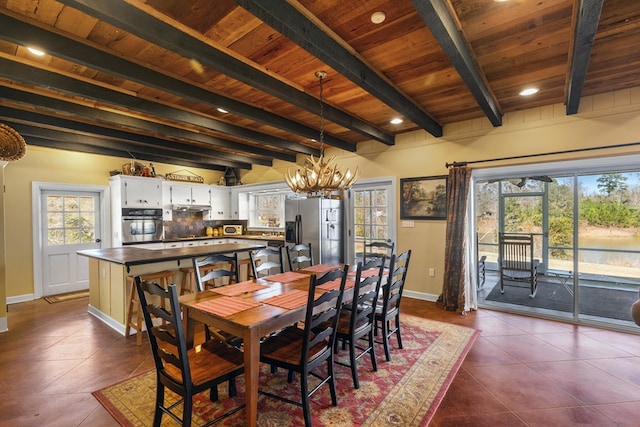 dining area featuring a chandelier, beam ceiling, dark tile patterned floors, and wooden ceiling