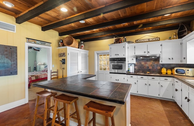 kitchen featuring stainless steel oven, a breakfast bar, beamed ceiling, white cabinets, and tile counters