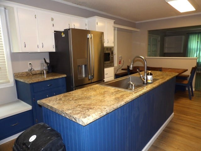 kitchen with stainless steel appliances, blue cabinets, sink, white cabinetry, and light hardwood / wood-style flooring