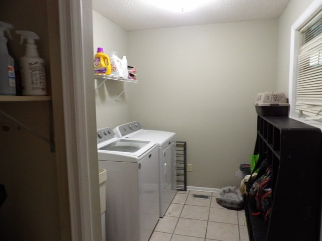 laundry area with a textured ceiling, light tile patterned flooring, and washing machine and clothes dryer