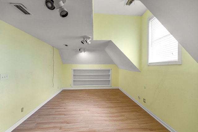 additional living space with wood finished floors, baseboards, visible vents, and built in shelves