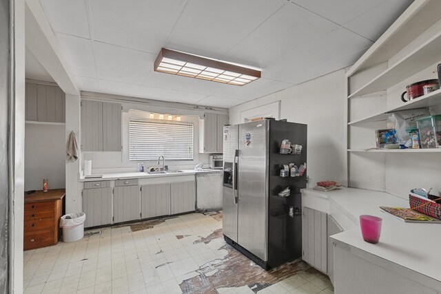 kitchen featuring a sink, light floors, open shelves, stainless steel fridge, and light countertops