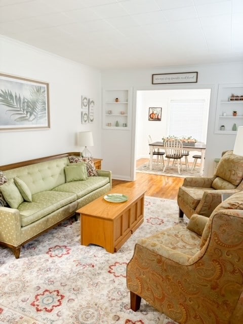 living room with built in shelves, light hardwood / wood-style floors, and crown molding