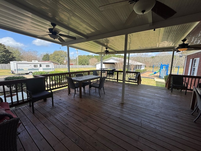 deck with outdoor dining space, a playground, fence, and an outdoor structure