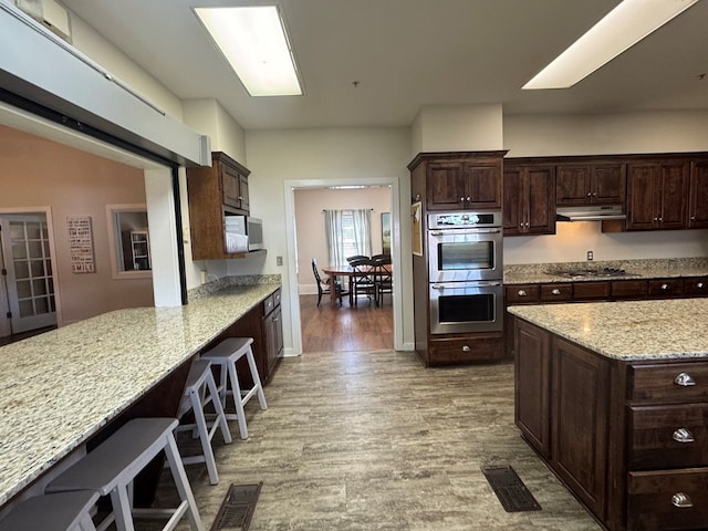 kitchen with visible vents, appliances with stainless steel finishes, dark brown cabinets, wood finished floors, and under cabinet range hood