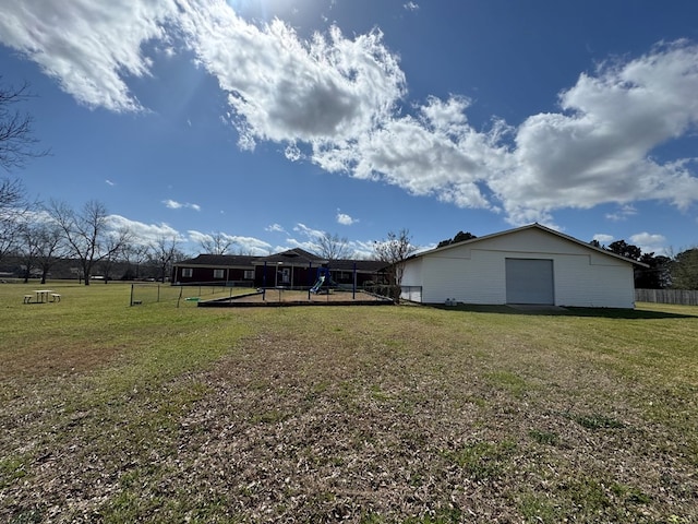 view of yard with a garage, fence, a playground, and an outbuilding